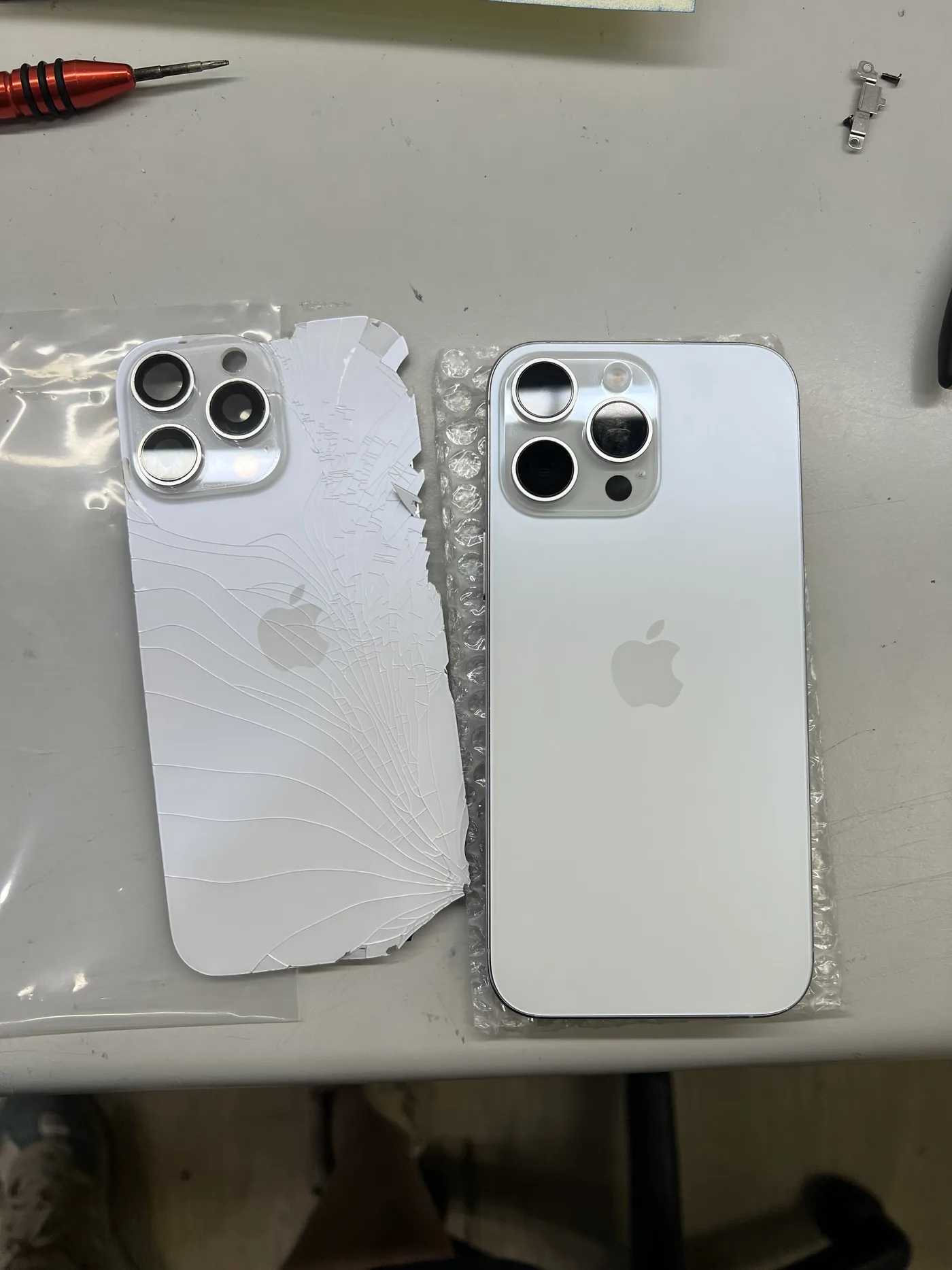 iPhone 16 Pro Max 拆下的整片破裂舊背蓋與新背蓋並排對照，舊背蓋裂痕從右下角放射