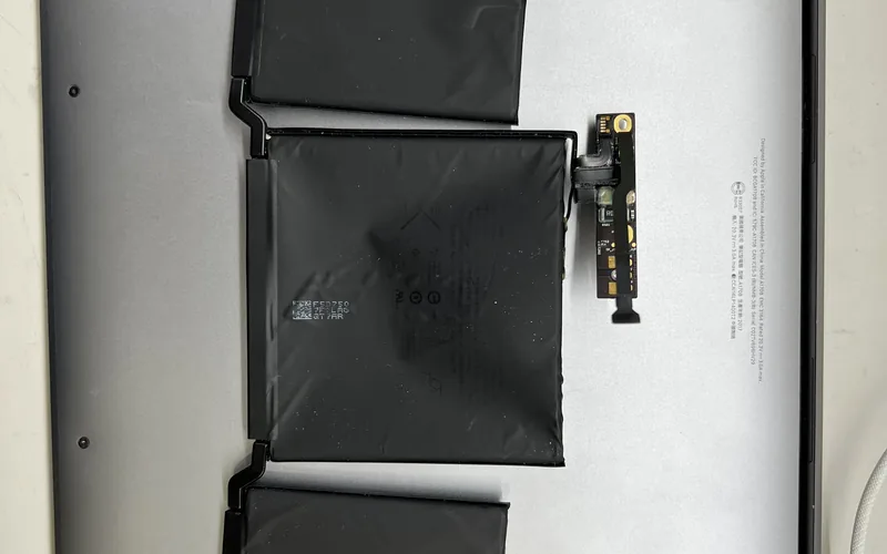 MacBook Pro A1708 拆下的舊電池，三組電芯與右側獨立的電池控制小板放在機身底殼上