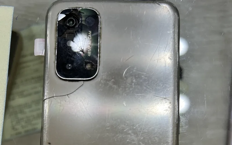 OPPO A74 背面，鏡頭模組玻璃碎裂並向下延伸出一道裂痕，機身表面佈滿摩擦刮痕