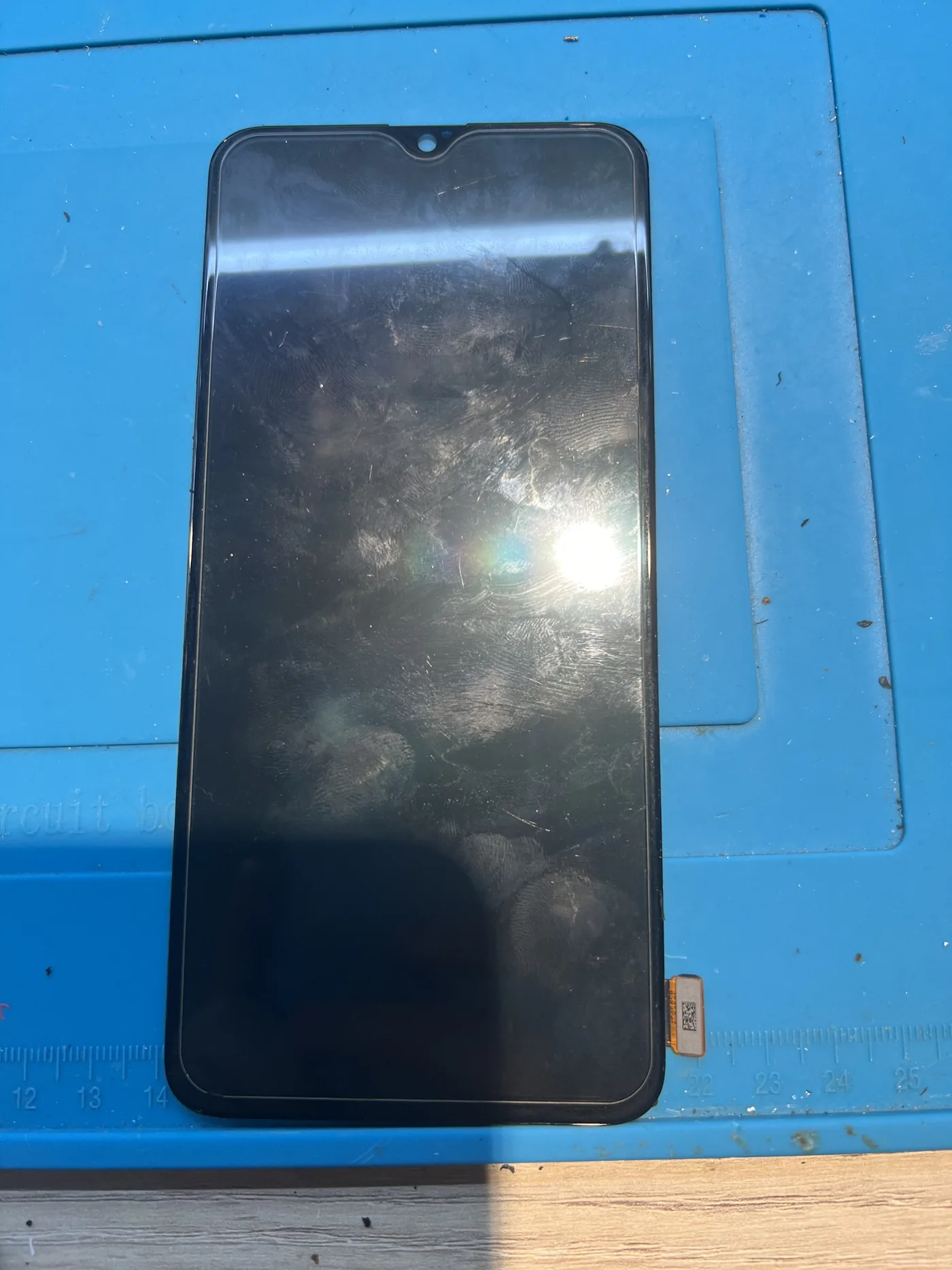 OPPO Reno5 更換用的螢幕總成放在藍色維修墊上，可見水滴型前鏡頭缺口與底部排線