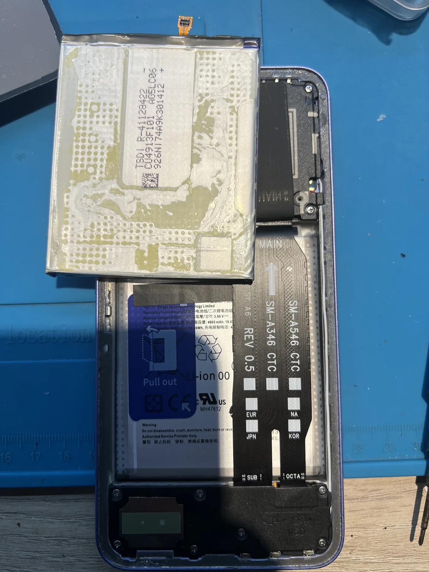 Samsung Galaxy A54 拆開背蓋更換電池，舊電池背面布滿殘膠，機身內已裝上新電池，排線印有 SM-A546