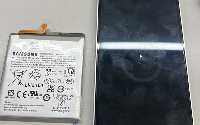 Samsung Galaxy S23 FE 換下的舊電池放在一旁，手機接上充電線後畫面顯示充電中圖示