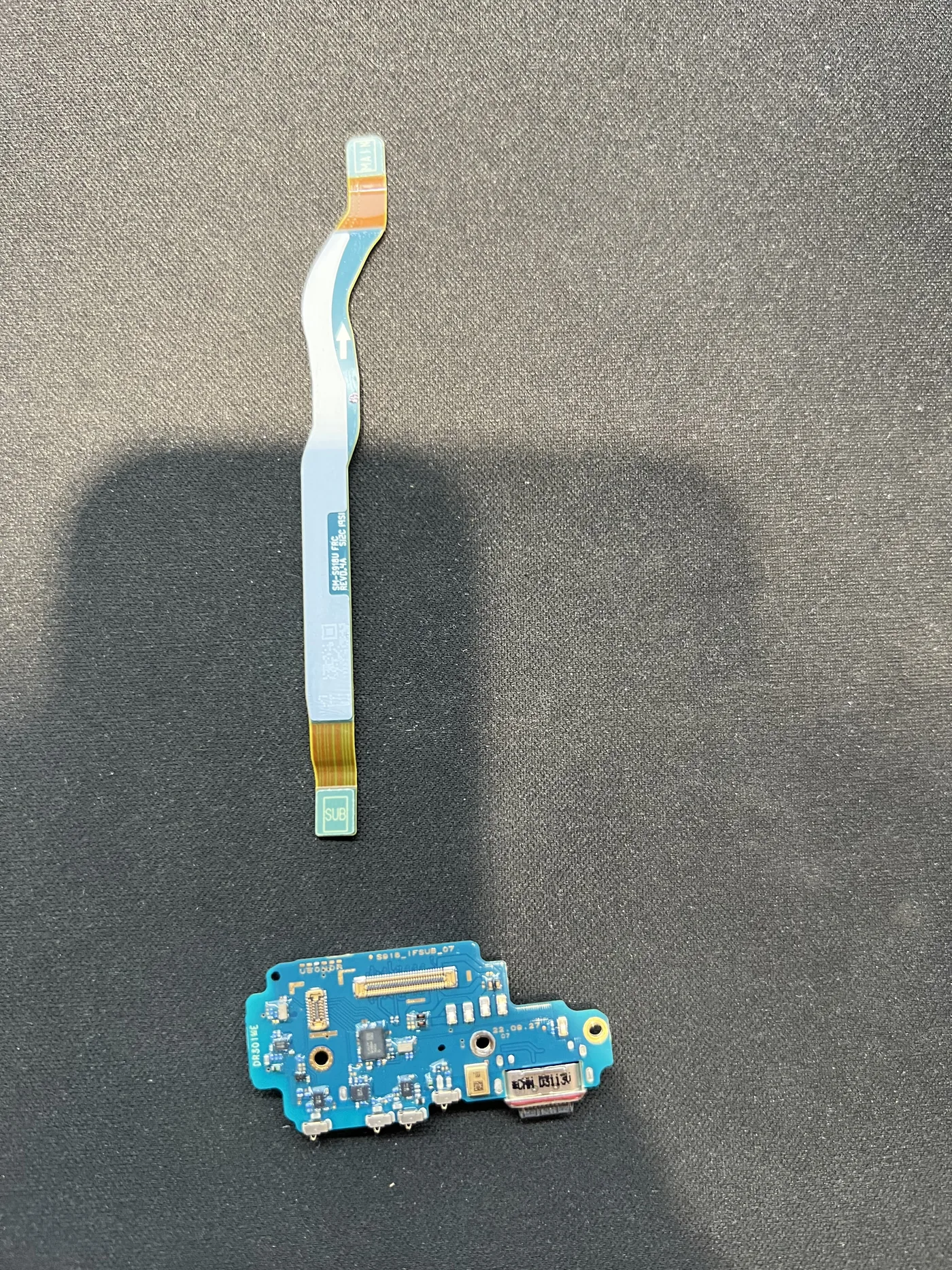 Samsung Galaxy S23 Ultra 拆下的尾插小板與主副板連接排線，放在深色維修墊上